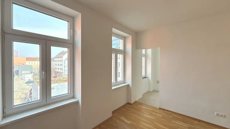 Helles, leeres Zimmer mit Parkettboden und großen Fenstern, bereit zur individuellen Gestaltung.