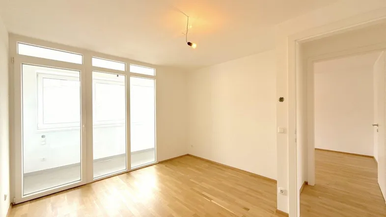 Helles, leeres Zimmer mit Parkettboden und Zugang zu einem Balkon, ideal für Wohn- oder Schlafbereich.