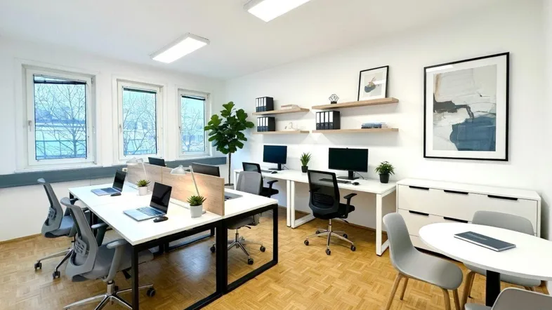 Helles, modernes Büro mit mehreren Arbeitsplätzen, großen Fenstern und Holzparkettboden.