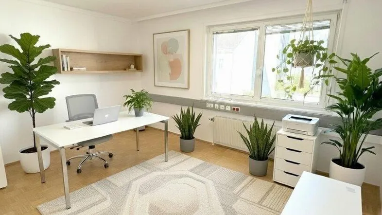 Helles und modernes Büro mit großem Schreibtisch, Pflanzen und einem gemusterten Teppichboden.