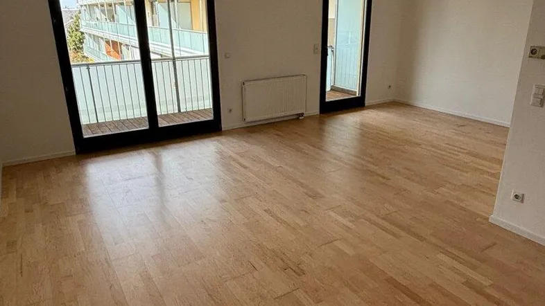 Helles Wohnzimmer mit Parkettboden und Zugang zu einem Balkon, ideal für natürliche Belichtung.