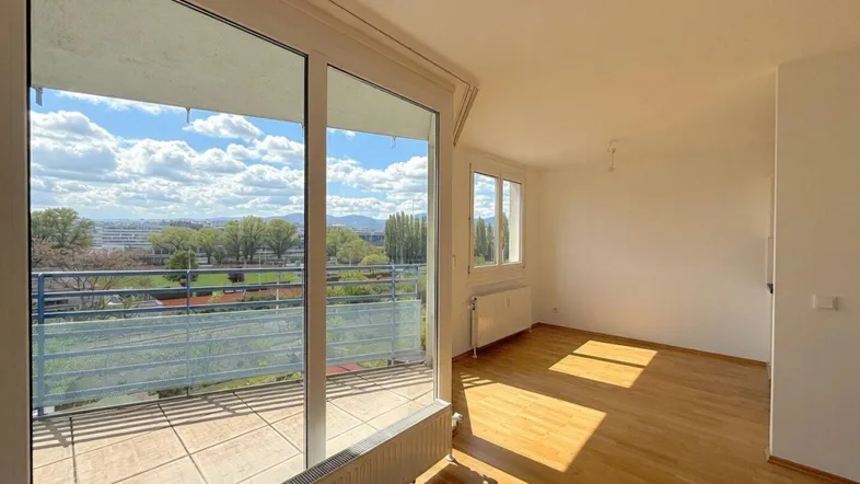 Lichtdurchfluteter Raum mit Holzboden und Zugang zu einem großen Balkon.