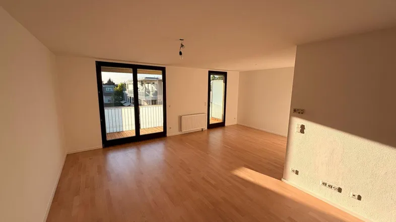 Helles, leeres Wohnzimmer mit Parkettboden und Zugang zu zwei Balkonen, gut beleuchtet.
