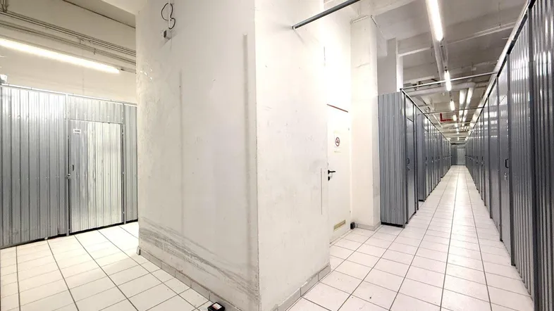 Langer Korridor in einer Lagerhalle mit vielen individuellen Stahllagereinheiten und Fliesenboden unter Leuchtstoffröhren.