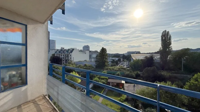 Sonniger Balkon mit blauem Geländer und weitem Blick über die Stadt und grüne Umgebung.