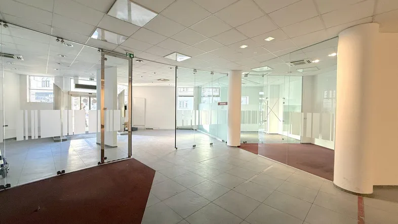 Geräumiger, leerer Gewerberaum mit modernen Glasabtrennungen, Fliesenboden und abgehängter Decke.