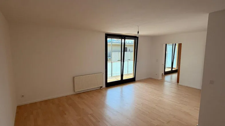 Helles Wohnzimmer mit Parkettboden, Heizkörper und Zugang zu einem Balkon.