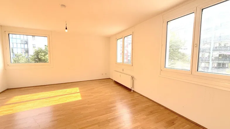 Helles Wohnzimmer mit Parkettboden und mehreren Fenstern, das viel Tageslicht hereinlässt.