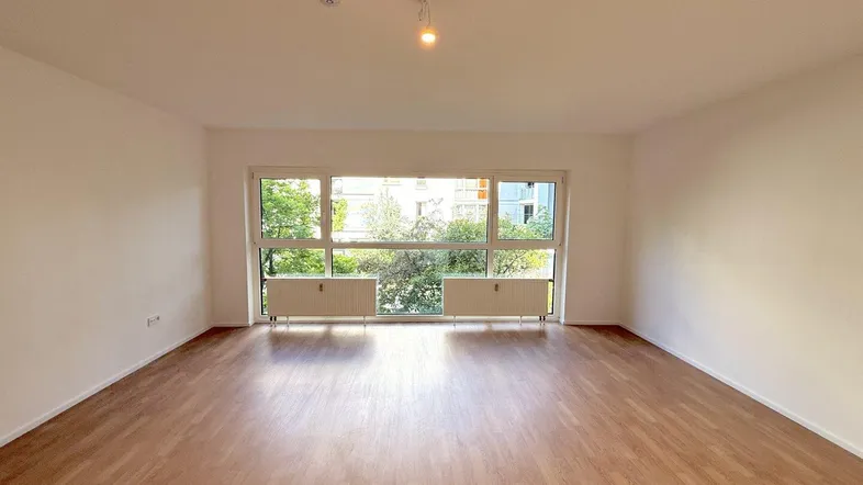 Helles Wohnzimmer mit großen Fenstern, Laminatboden und Blick ins Grüne.