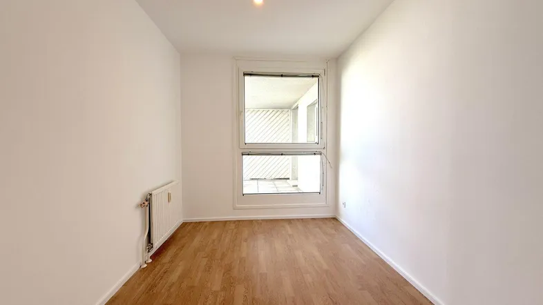 Helles Zimmer mit Laminatboden und Fenster, das viel Tageslicht hereinlässt.