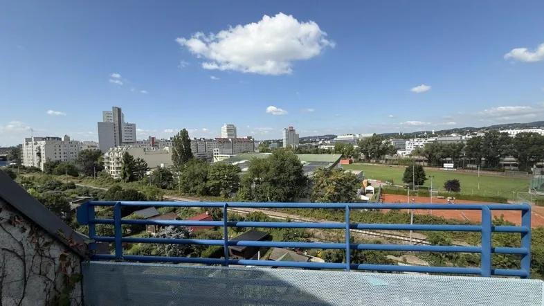 Weitblick von der Terrasse über die Stadt mit Sportplätzen und Gebäuden unter blauem Himmel.
