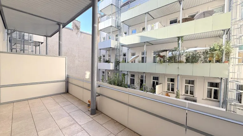 Geräumiger Balkon mit Fliesenboden und Blick auf die umliegenden Gebäude und Grünflächen.