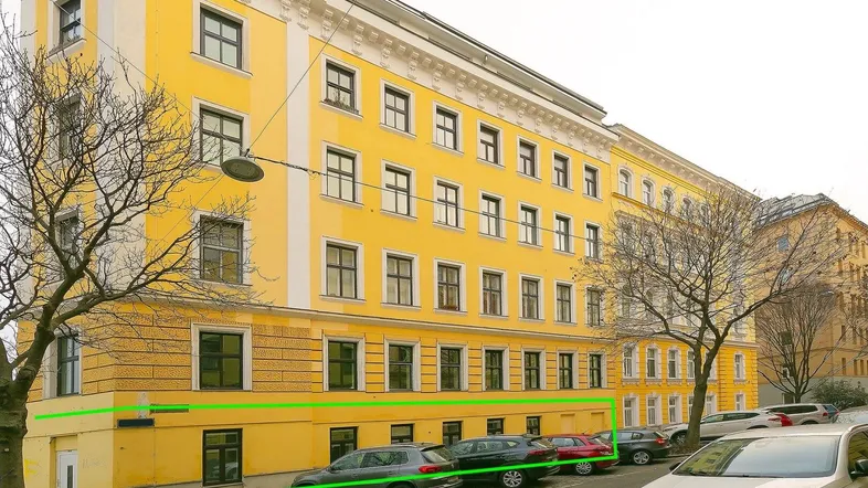 Gelbes Mehrfamilienhaus mit klassischer Architektur und parkenden Autos an der Straße.