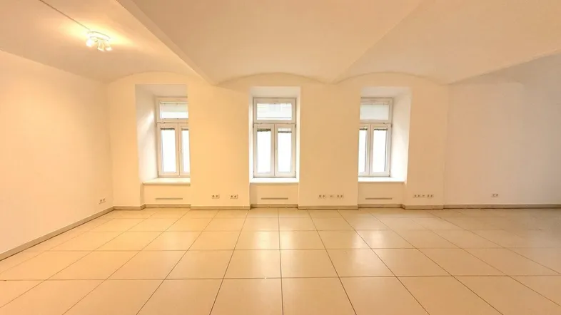Geräumiger, leerer Raum mit hellen Fliesen, drei Fenstern und gewölbter Decke.
