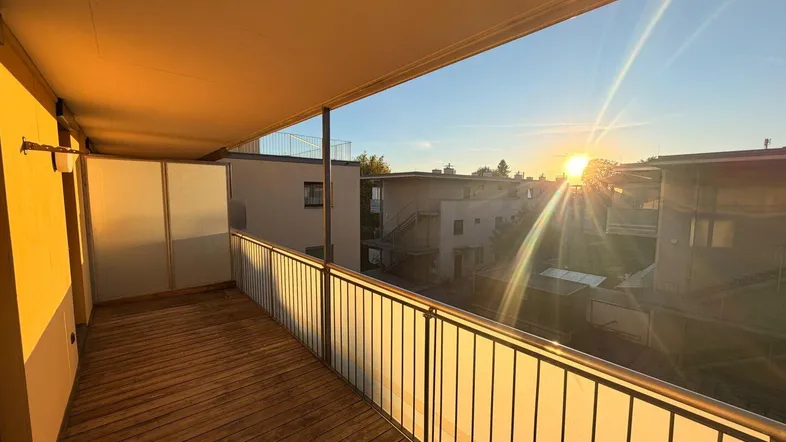 Geräumiger Balkon mit Holzboden und Blick auf die umliegenden Gebäude bei Sonnenuntergang.