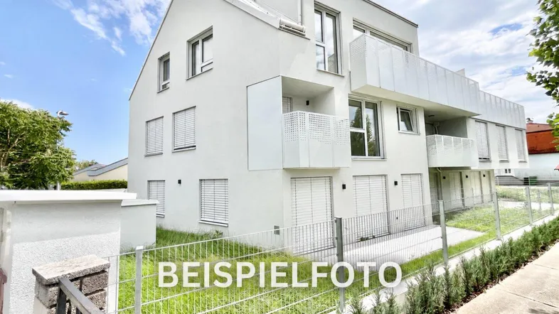 Modernes weißes Mehrfamilienhaus mit Balkonen und großen Fenstern in einer grünen Umgebung.