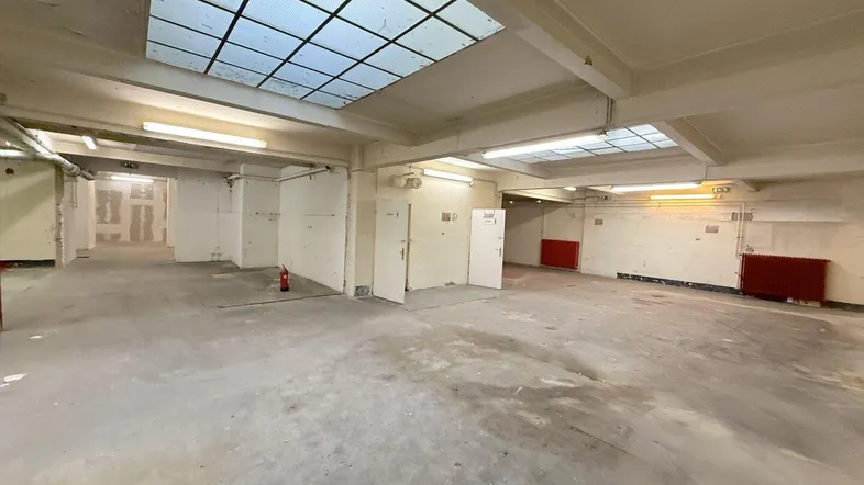 Großer, leerer Gewerberaum mit Betonboden, Oberlichtern und sichtbaren Installationen, bereit für den Ausbau.