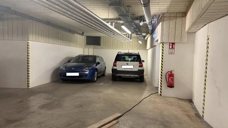Tiefgarage mit zwei geparkten Autos, sichtbaren Rohren an der Decke und Betonboden.