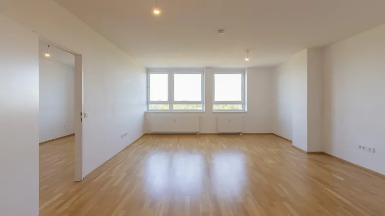 Helles, leeres Wohnzimmer mit großen Fenstern und Parkettboden, bereit zur individuellen Gestaltung.