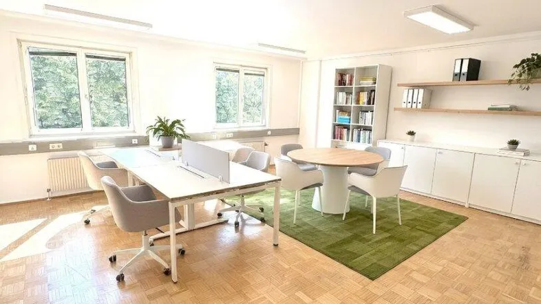 Modernes Büro mit mehreren Arbeitsplätzen, Konferenztisch und Blick ins Grüne durch große Fenster.