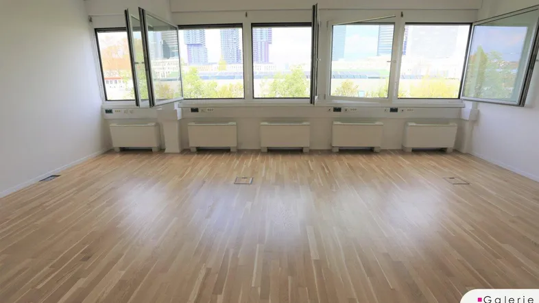 Heller Büroraum mit Holzboden und einer Reihe von Fenstern, die einen weiten Blick auf die städtische Umgebung ermöglichen.