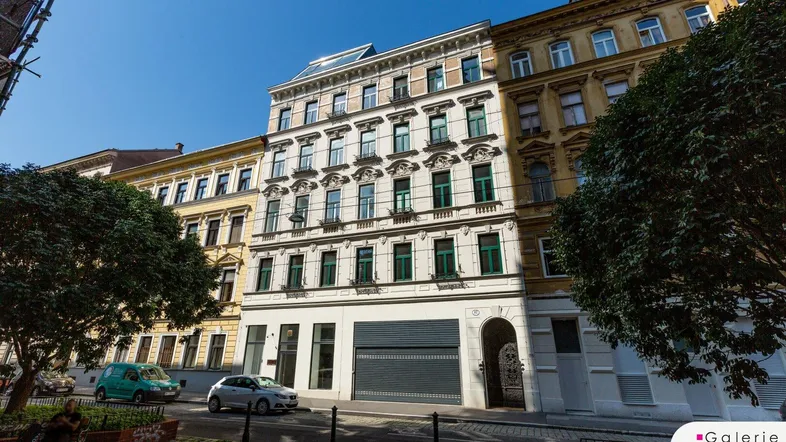 Historisches Gebäude in einer belebten Straße mit Bäumen und parkenden Autos.