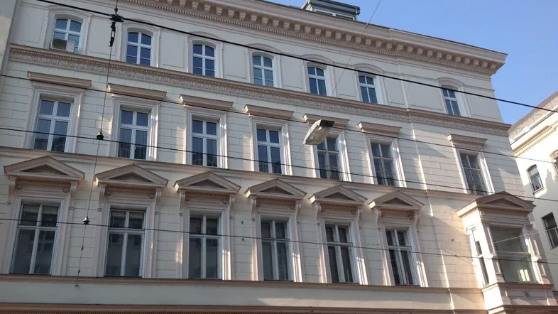 Klassische Fassade eines Altbaus mit vielen Fenstern und dekorativen Elementen unter blauem Himmel.
