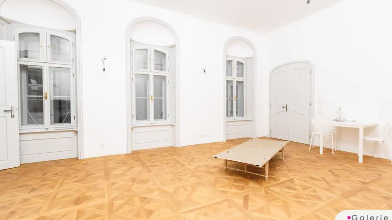 Geräumiger Raum mit elegantem Parkettboden, hohen Bogenfenstern und viel natürlichem Licht.