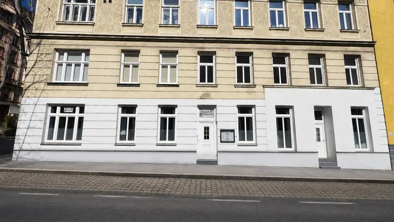 Fassade eines Mehrfamilienhauses mit mehreren Etagen und Geschäften im Erdgeschoss.