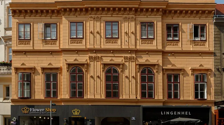 Detailansicht der historischen Fassade mit reich verzierten Fenstern und zwei Ladenlokalen im Erdgeschoss.