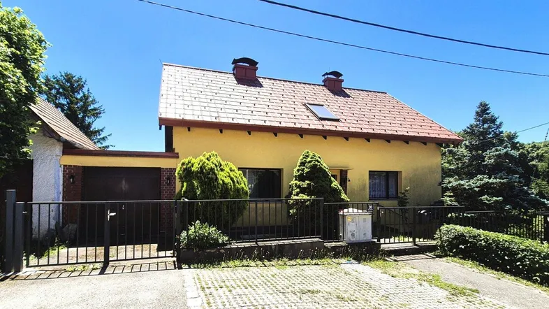 Gelbes Einfamilienhaus mit rotem Ziegeldach, Vorgarten und Einfahrt an einem sonnigen Tag.