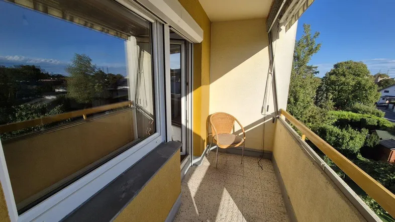 Heller Balkon mit Terrazzoboden, einem Stuhl und Blick ins Grüne.