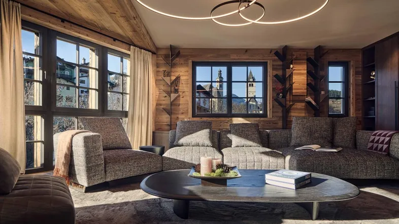 Gemütliches Wohnzimmer im alpinen Stil mit Holzwänden, großen Fenstern und moderner Beleuchtung.