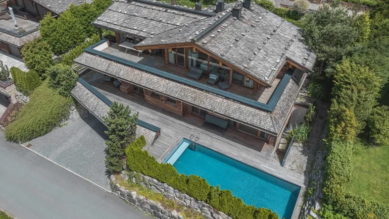 Luxuriöses Holzhaus mit traditionellem Schindeldach, großzügiger Terrasse und privatem Außenpool in alpiner Umgebung.