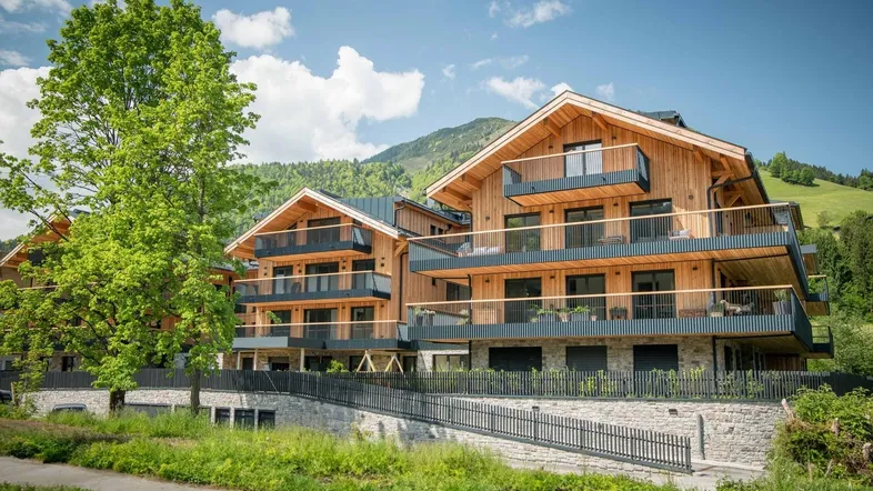 Attraktives Mehrfamilienhaus in Holzbauweise mit mehreren Balkonen, eingebettet in grüne Hügellandschaft.