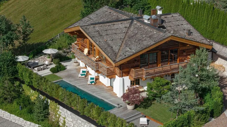 Luftaufnahme eines luxuriösen Chalets mit Pool, Holzterrasse und gepflegtem Garten in alpiner Umgebung.