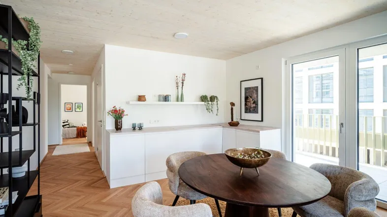 Heller offener Wohnbereich mit Parkettboden, Holzbalkendecke und Zugang zu einem Balkon.