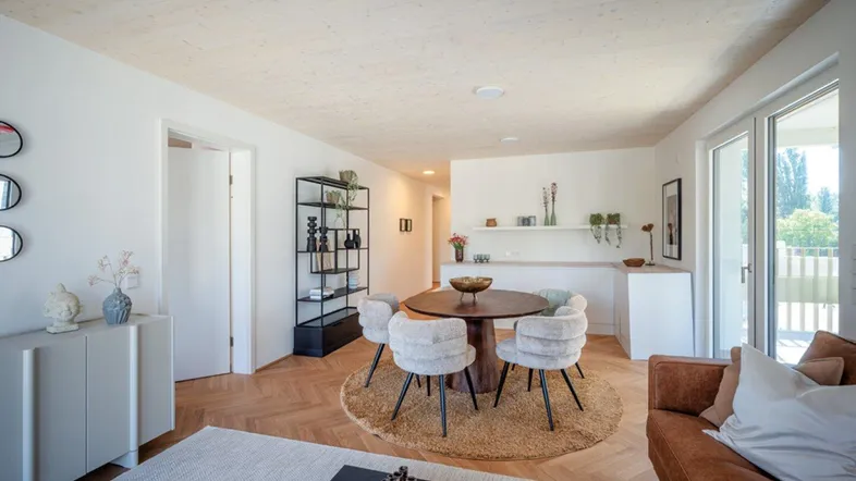 Heller, offener Wohn- und Essbereich mit Parkettboden, Holzbalkendecke und Zugang zum Balkon.