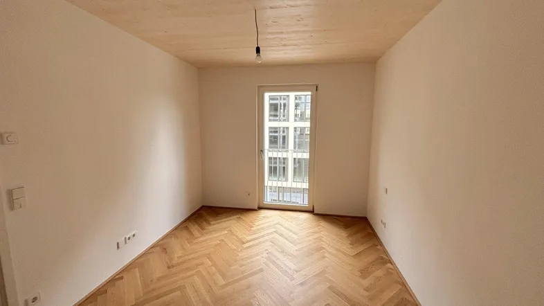 Helles Zimmer mit Fischgrätparkettboden und Zugang zu einem französischen Balkon.