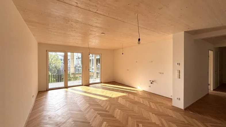 Helles Wohnzimmer mit Fischgrätparkett, Holzdecke und Zugang zum Balkon, in neuwertigem Zustand.
