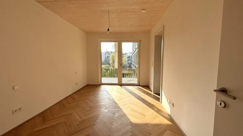 Helles Zimmer mit Fischgrätparkett, Holzbalkendecke und Zugang zu einem Balkon.