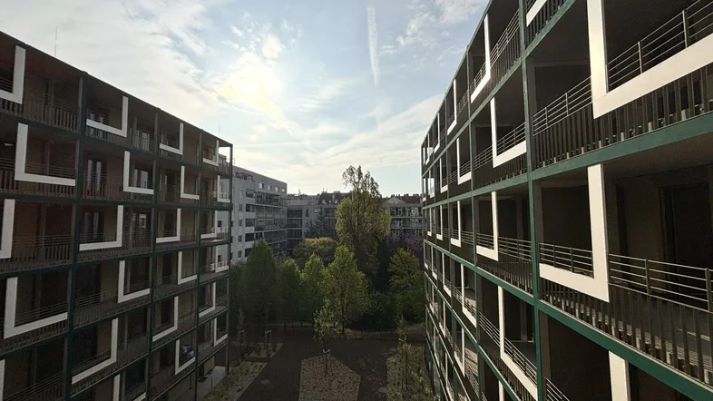 Moderne Wohngebäude mit Balkonen und einem begrünten Innenhof unter blauem Himmel.