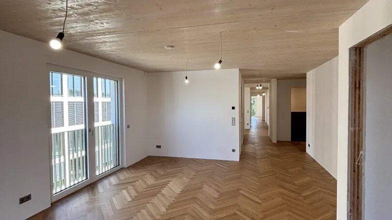 Geräumiger Wohnbereich mit elegantem Fischgrätparkett und einer Decke aus hellem Holz.