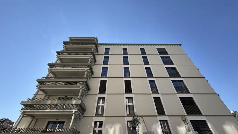 Moderne Gebäudefassade mit Balkonen und großen Fenstern unter blauem Himmel.