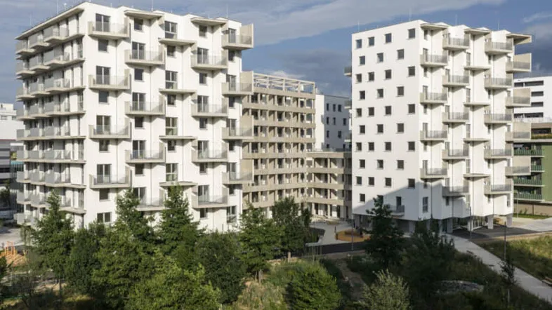 Moderne Wohngebäude mit zahlreichen Balkonen und umgebender Grünfläche unter bewölktem Himmel.