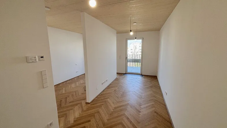 Helles, unmöbliertes Zimmer mit Fischgrätparkett und Zugang zu einem Balkon.