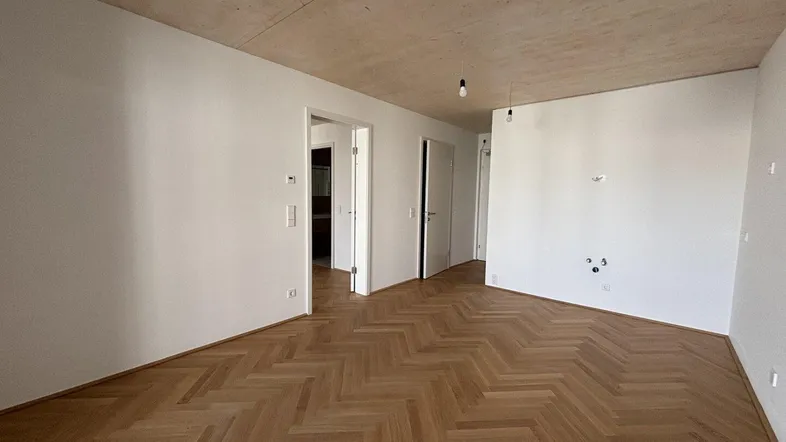 Leerer Raum mit Fischgrätparkettboden, weißen Wänden und einer Holzdecke, bereit zur individuellen Gestaltung.