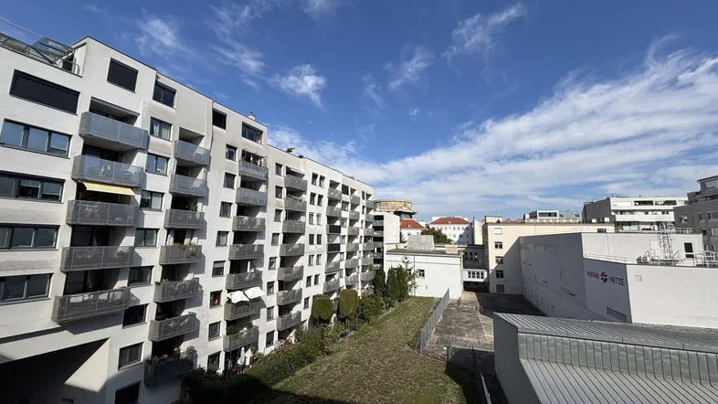 Modernes Wohngebäude mit zahlreichen Balkonen und Blick auf die umliegende Stadtlandschaft unter blauem Himmel.