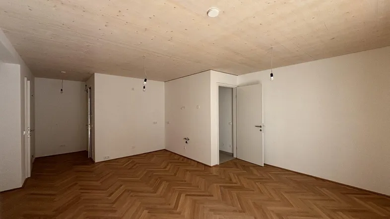Helles Zimmer mit Fischgrätparkett und Holzbalkendecke, bereit für die individuelle Gestaltung.