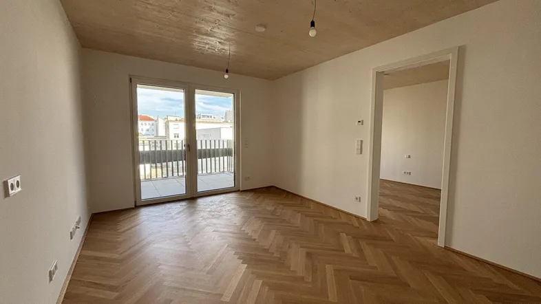Helles Wohnzimmer mit Fischgrätparkettboden und Zugang zu einem Balkon in einem Neubau.
